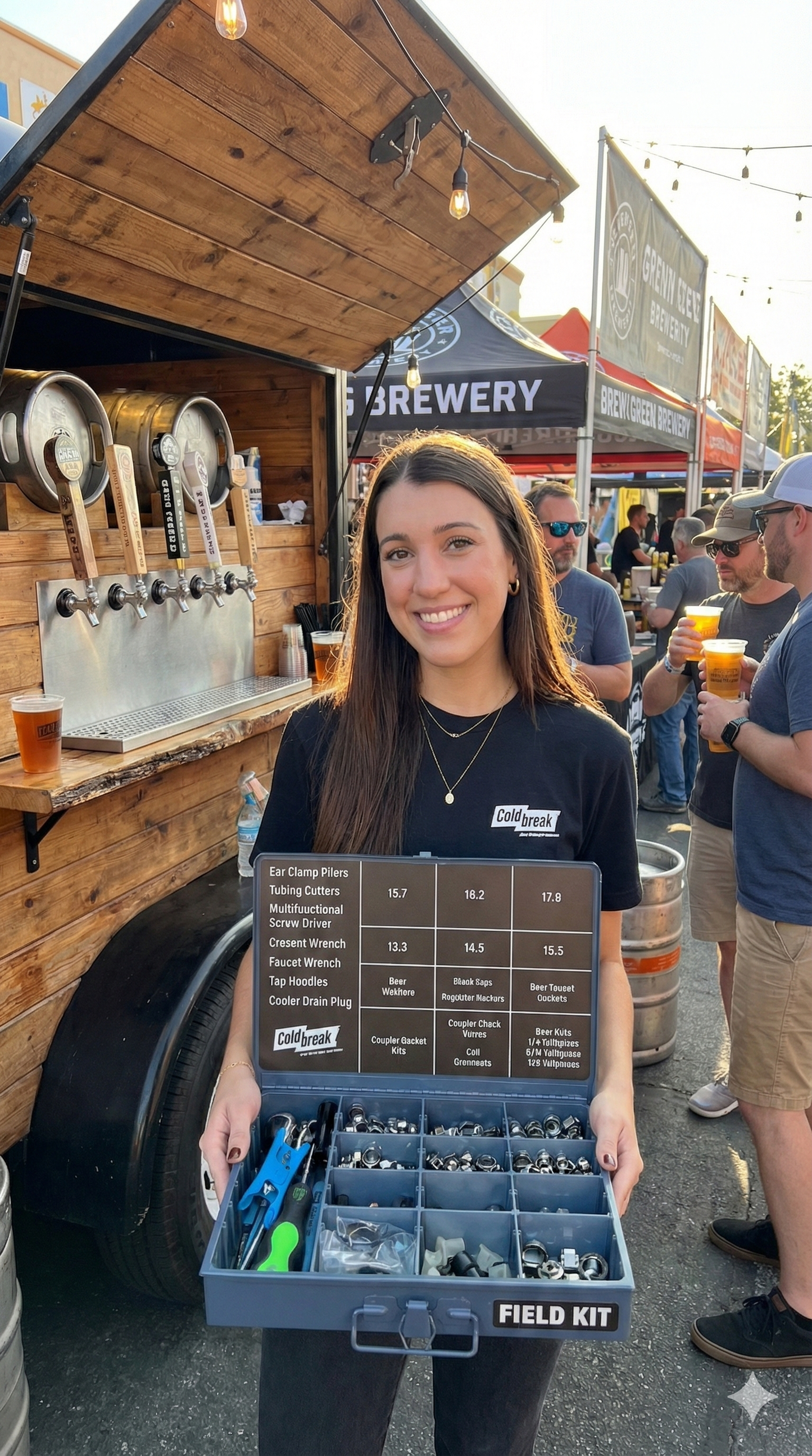 Woman in a black coldbreak t-shirt holding a field kit in front of a wooden truck with beer taps and people in the background.