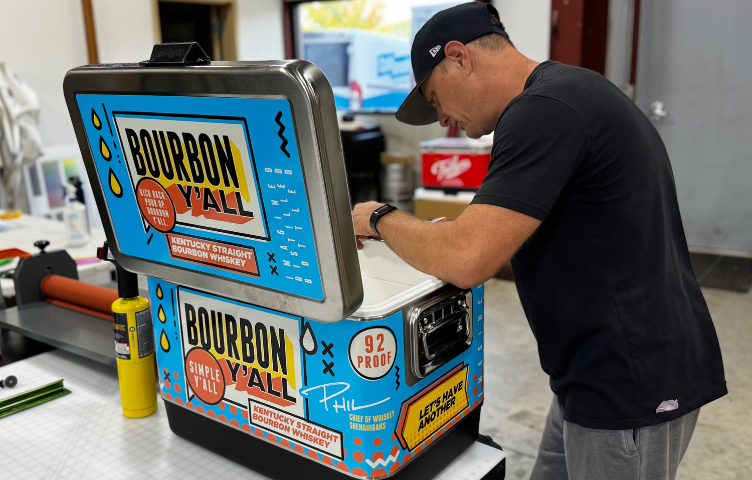 Person working on a colorful machine with 'Bourbon Y'all' branding in an indoor setting. Jockey Box cooler wrap by Coldbreak.